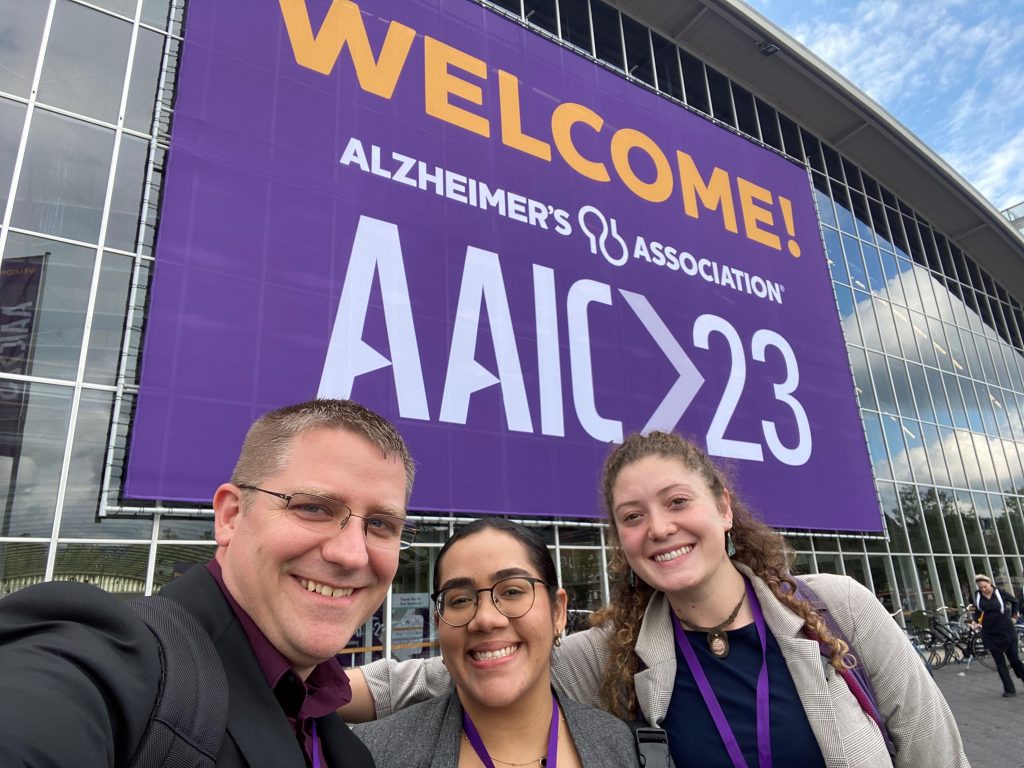 Left to Right: Tobey Betthauser, Erica Irizarry Pagan, and Jordan Teague standing in front of "Welcome" sign at AAIC 2023.