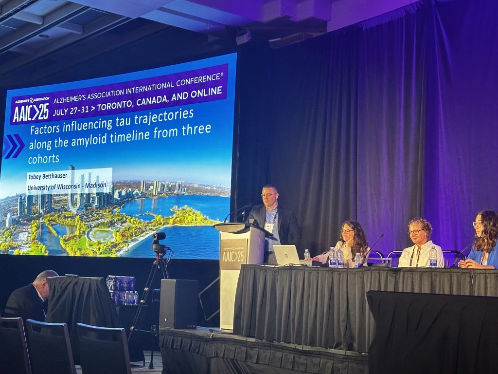 Dr. Tobey Betthauser at podium next to title slide of presentation.