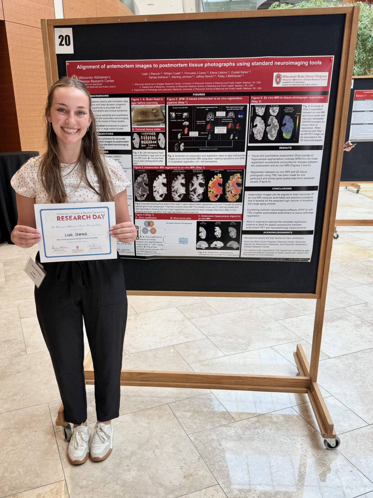 Leah Staruck holding Best Undergraduate Student Poster Award in from of Research Poster at ADRD 2026. 